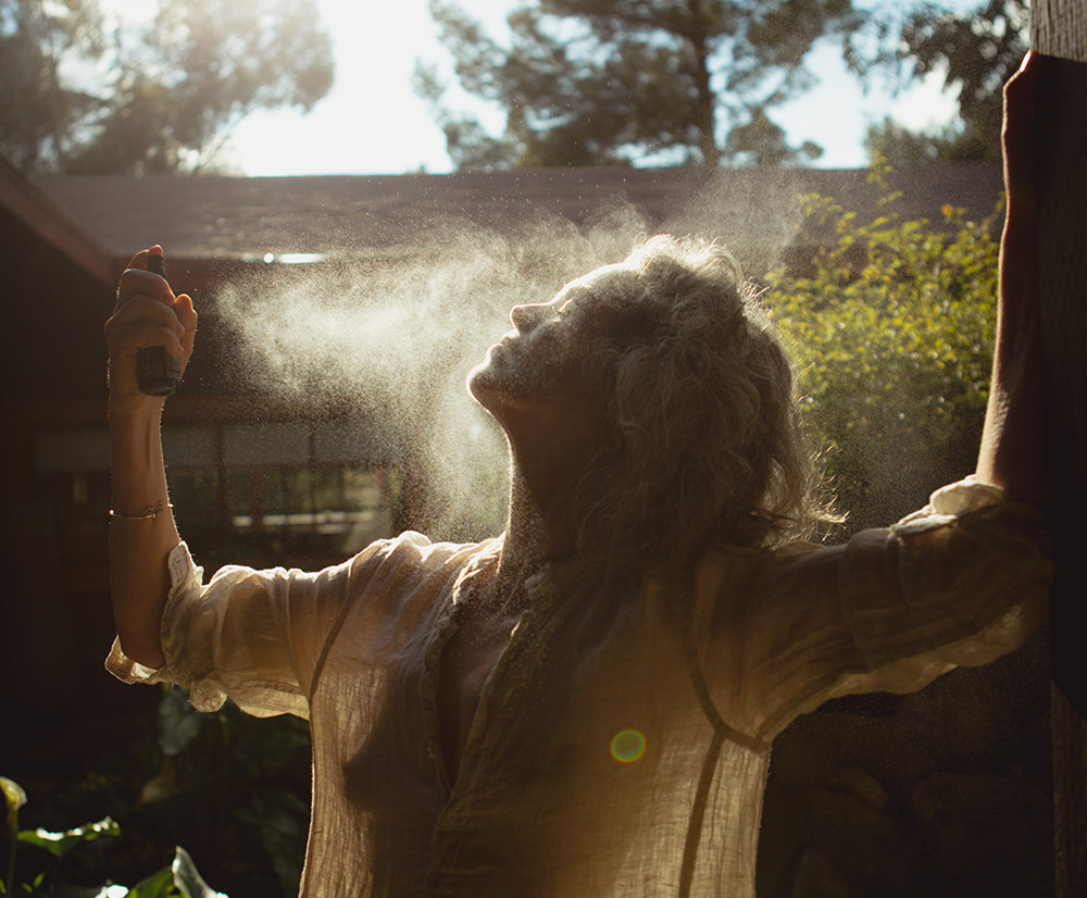 woman spraying hydrosol mist on face in sunlight